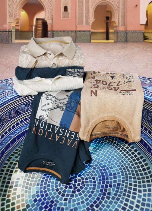 T-Shirts und Poloshirts liegen ordentlich gefaltet auf einem Brunnen mit Mosaikoptik. im Hintergrund sieht man einen Vorhof in einer orientalischen Region.