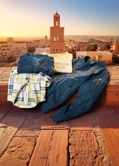 T-Shirts, ein Hemd und eine Jacke liegen auf einer Mauer. Im Hintergrund sieht man eine orientalische Stadt.