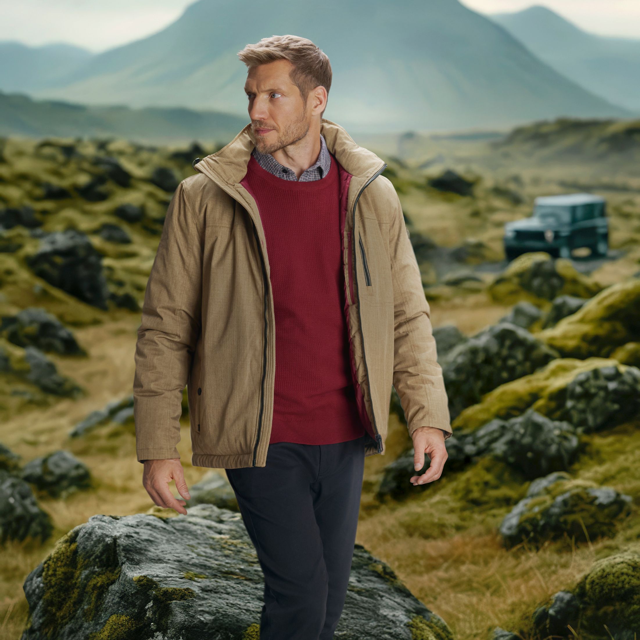 Mann in beiger Outdoorjacke und rotem Pullover wandert durch grüne Felsenlandschaft