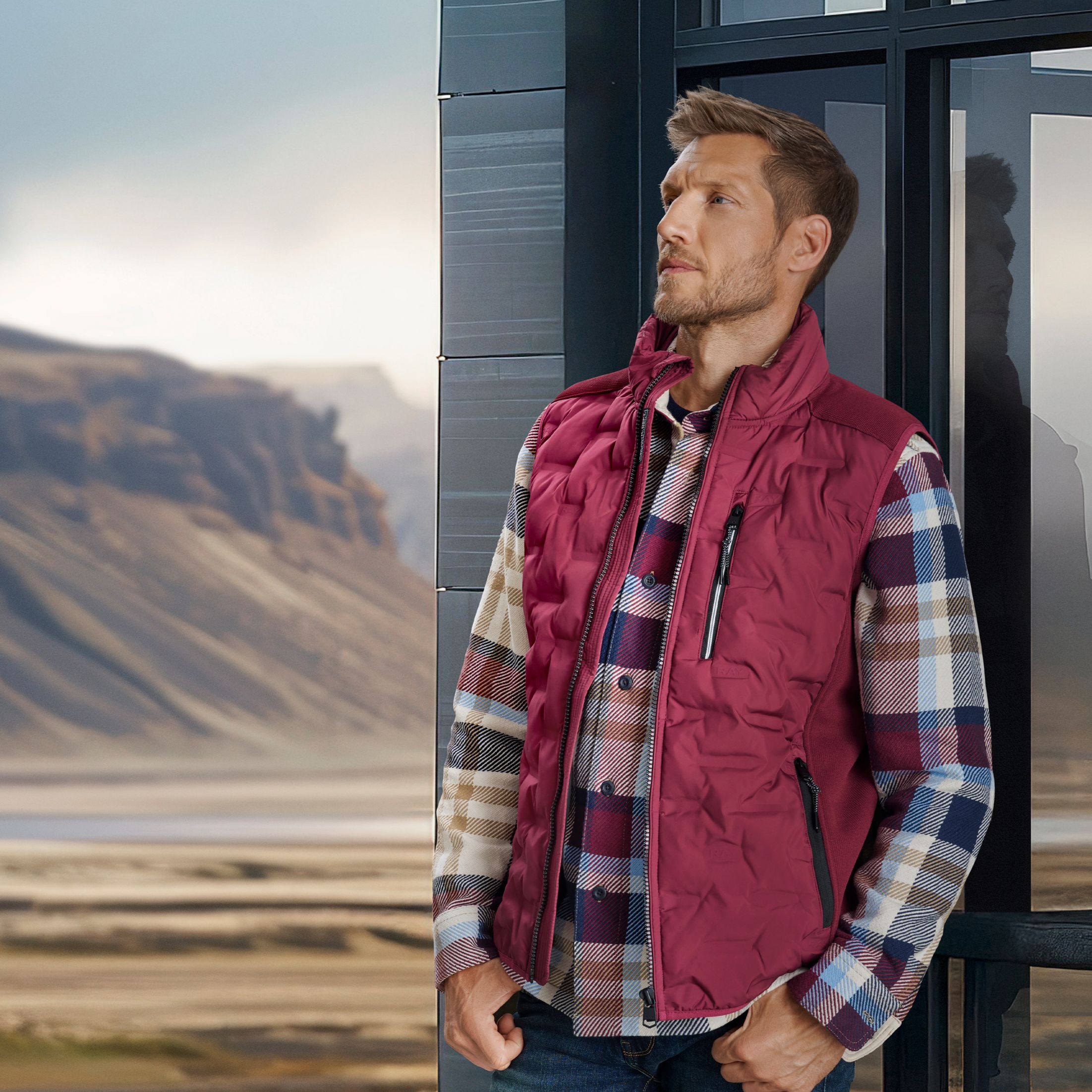 Herrenoutfit mit kariertem Hemd und roter Steppweste vor Berglandschaft