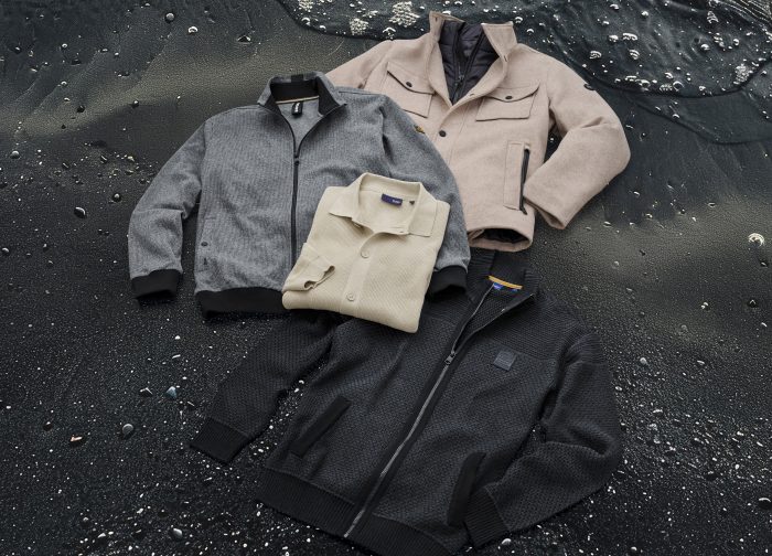Herrenmode Flatlay: vier Jacken und Pullover in neutralen Farben auf dunklem Hintergrund