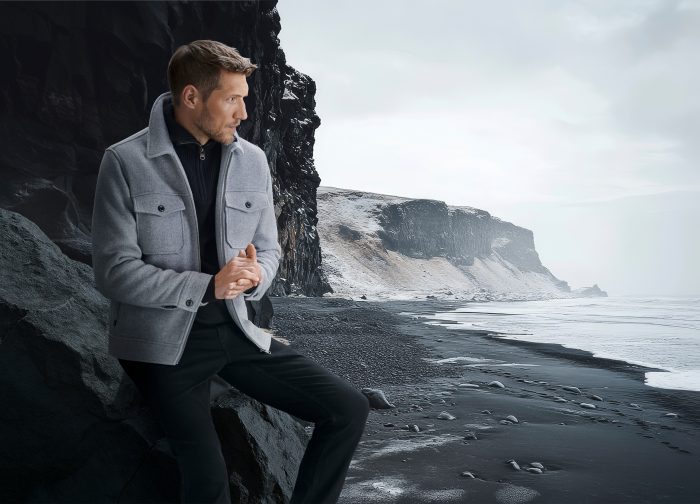 Model in grauer Outdoorjacke an schwarzem Sandstrand